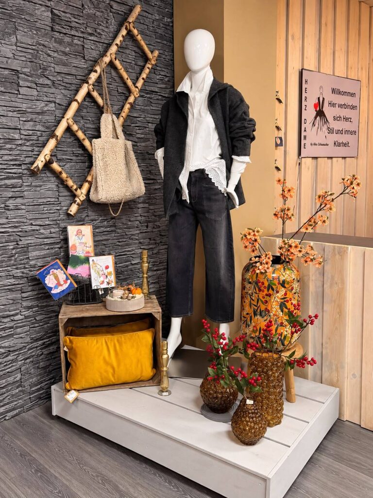 Schaufensterpuppe in Jeans und Blazer mit Herbstzweigen vor der Steinwand